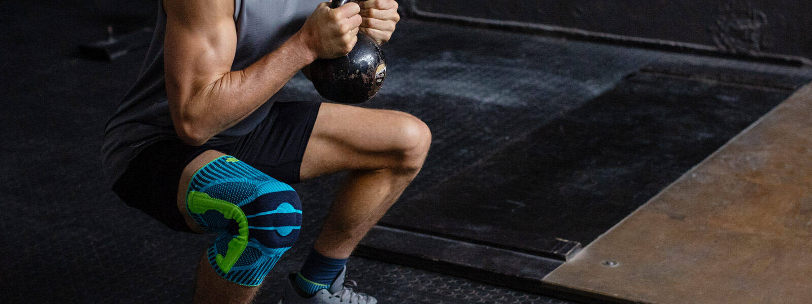 Il supporto per il ginocchio sportivo ti offre ottimi servizi, specialmente nell'allenamento di fitness L'uomo con un ginocchio va profondamente accovacciato con un kettlebell tra le due mani