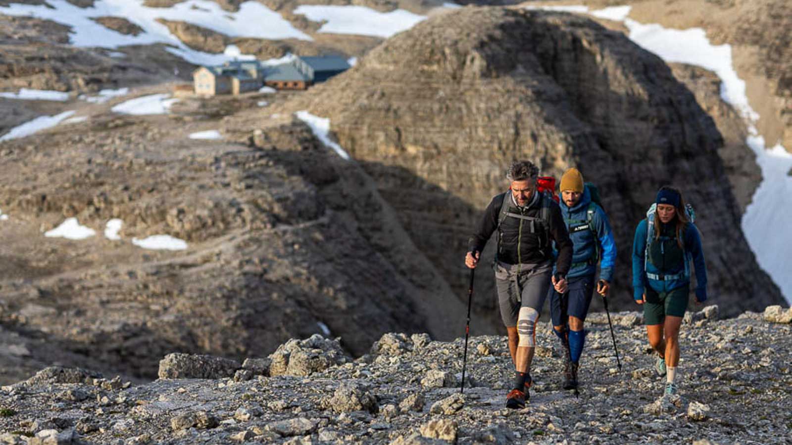 Bellissima escursione nelle Dolomiti Paesaggio roccioso nelle Dolomiti, con un gruppo di escursionisti in primo piano che indossano bendaggi e calze da escursionismo, e un rifugio alpino sullo sfondo.