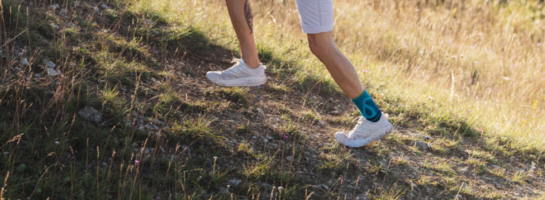 Achille Bandage Tendon Banda Rivera Trailrunning Sezione immagine di un uomo che corre su un prato collinare, indossa un bastone di tendine di Achille