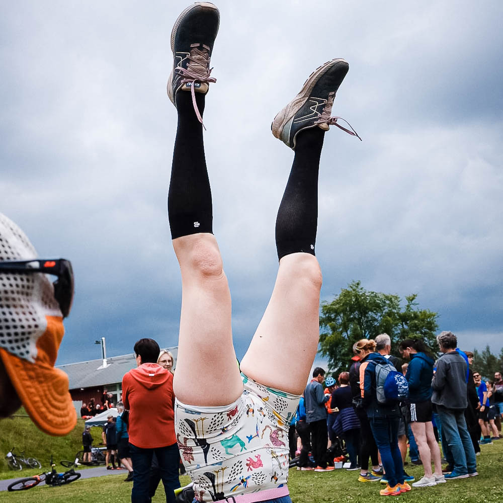 Un po' di divertimento dopo il torneo con le calze da recupero Bauerfeind Una donna con pantaloncini sportivi corti e calze al ginocchio fa la verticale