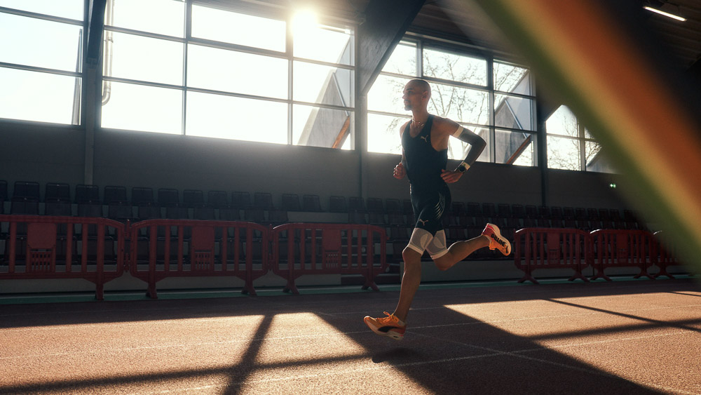 Il maratoneta Hendrik Pfeiffer si allena su una pista indoor controluce, indossando maniche e fasce compressive per stabilità e performance.