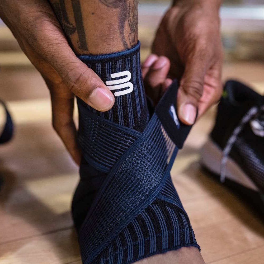 Primo piano di un supporto per caviglia nero con zone di supporto integrate e una fascia elastica per una regolazione personalizzata.