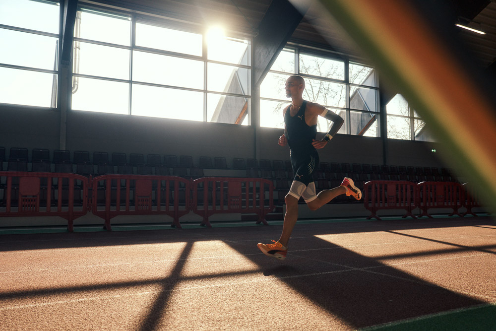 Il maratoneta Hendrik Pfeiffer si allena su una pista indoor controluce, indossando maniche e fasce compressive per stabilità e performance.