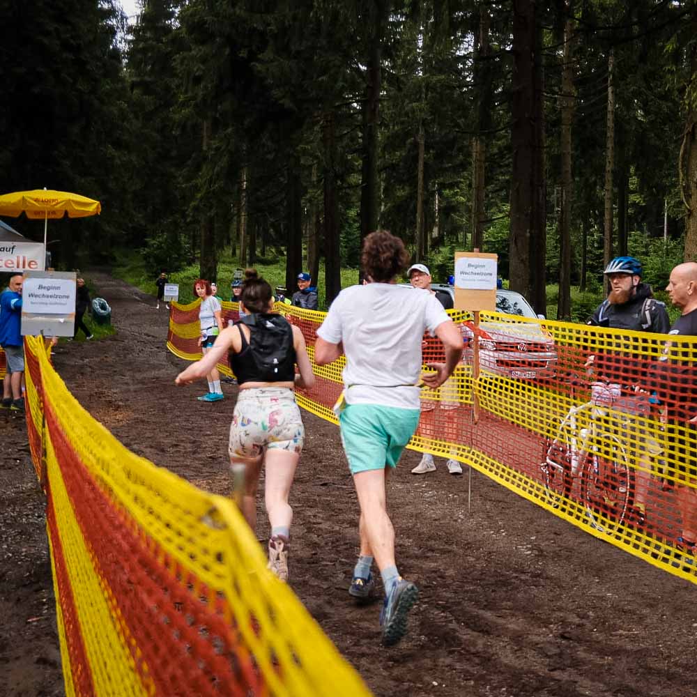 Staffetta mista attraverso il Rennsteig Un uomo e una donna camminano nella foresta, osservati dai passanti, mentre il terreno è fangoso