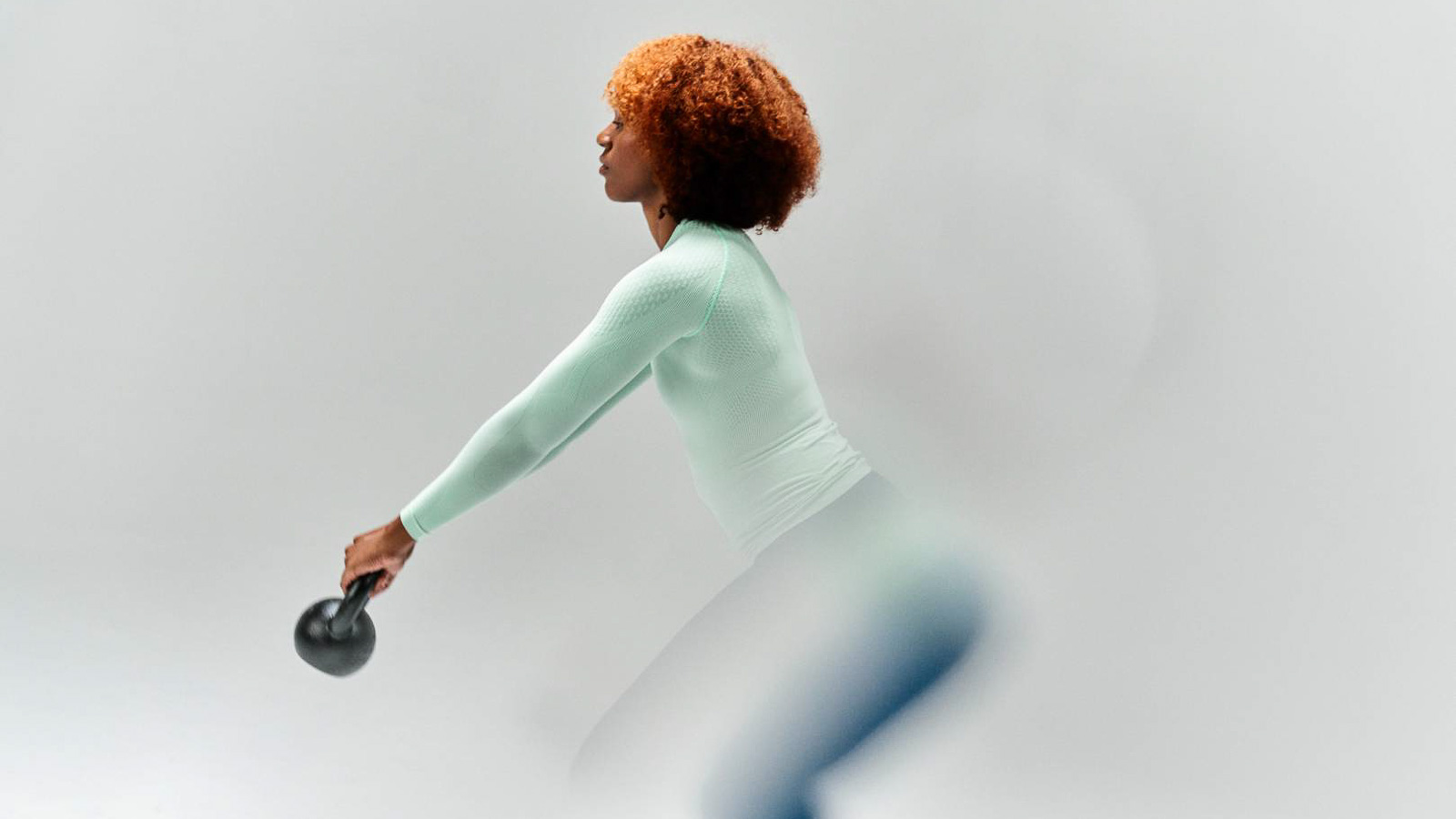 Allenamento efficace con stile - Esercizi con kettlebell in abbigliamento a compressione di alta qualità! Una donna in una maglia a compressione sports wear color menta esegue un esercizio con kettlebell. L'attenzione è rivolta al suo movimento e all'abbigliamento sportivo funzionale su uno sfondo neutro.