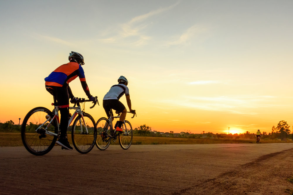 Anche la sera c'è una piccola uscita con la bici da corsa Due ciclisti da corsa guidano nel tramonto su una strada in cemento piatto