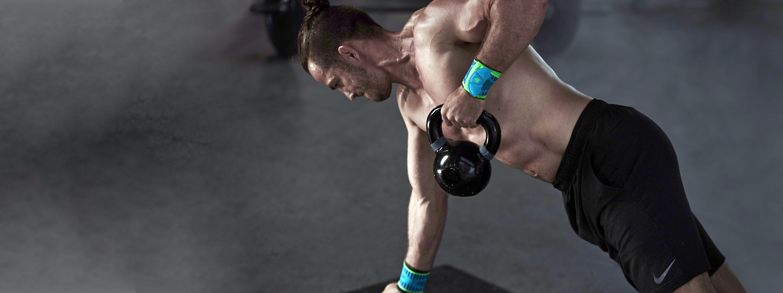 Allenamento di kettlebell - ancora più potente con il cinturino da polso sportivo L'uomo atletico con busto gratuito e bendaggi del polso si allena con il kettlebell che una mano supporta l'altra tira su il kettlebell