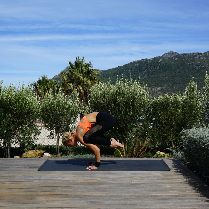 Yoga a casa con cinturino da polso sportivo La donna fa bilanciare lo yoga sulla sua terrazza sulle mani mentre le gambe pendono dietro la parte superiore del corpo in aria