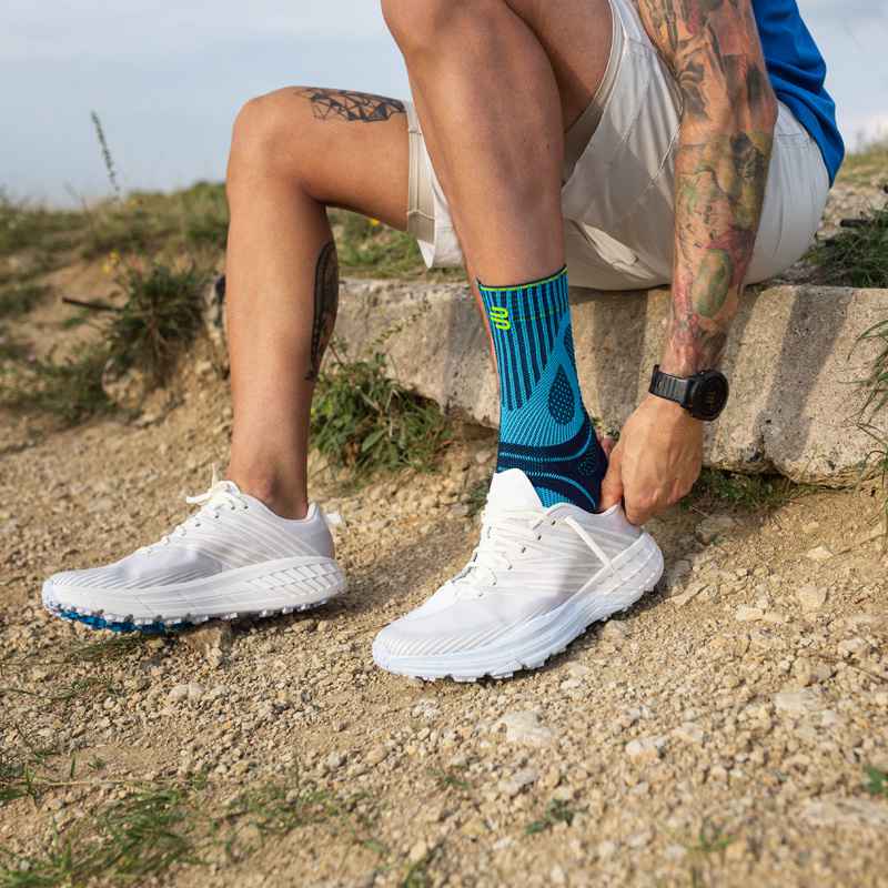 L'uomo tira una scarpa da corsa su una pietra su una pietra sopra la sua fascia di tendine di Achille