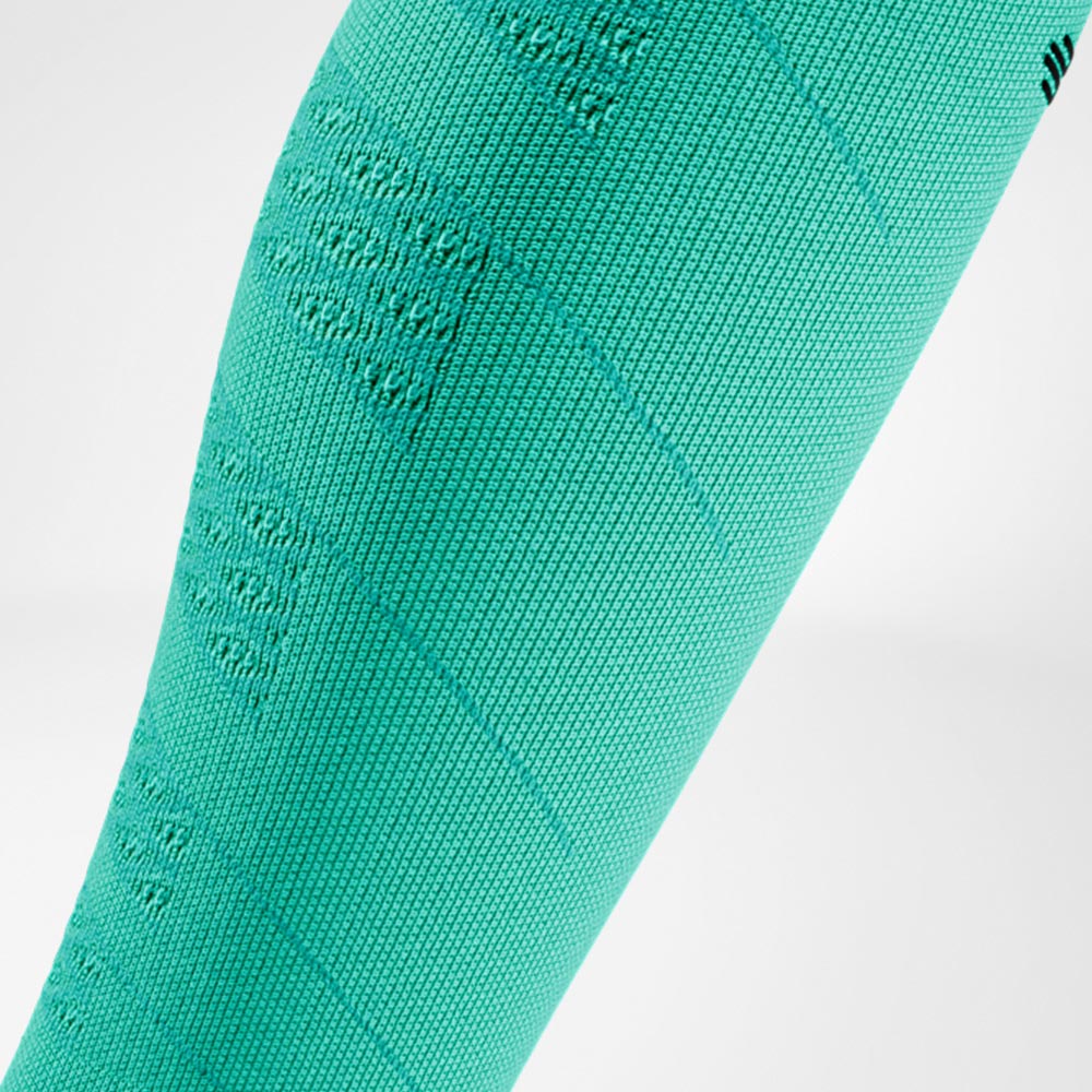 Dettaglio di una Run Performance Compression Sleeve verde sulla parte inferiore della gamba, con struttura a maglia ben visibile che garantisce compressione uniforme e supporto durante l’attività sportiva.