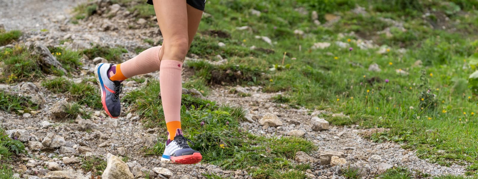 Trail Run Socks Peach in azione Il corridore corre giù per una montagna e indossa i calzini per pista nella pesca del colore