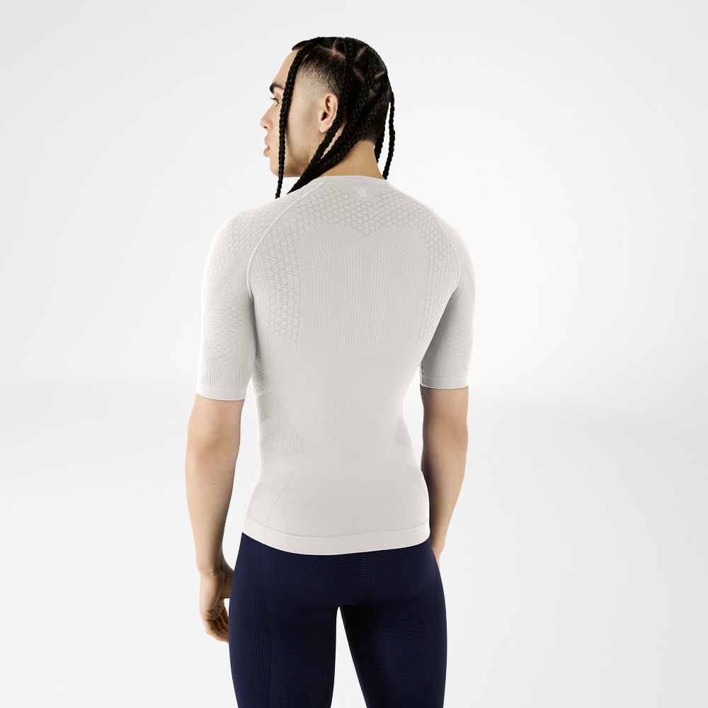 Un uomo indossa una maglia a compressione grigio argento, di spalle alla fotocamera, guarda oltre la spalla.