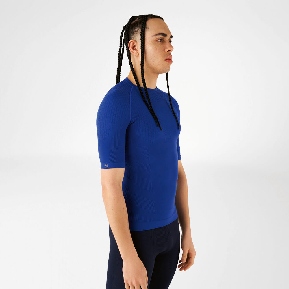 Un uomo indossa una maglia a compressione blu, sta di lato e guarda avanti.