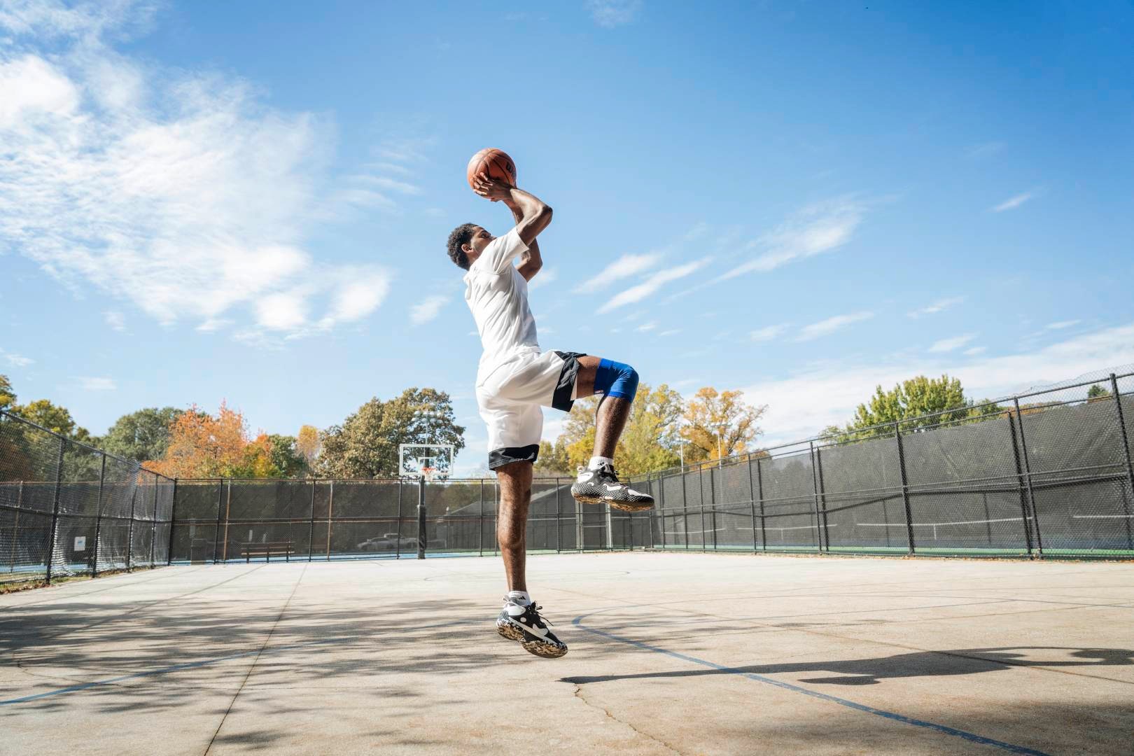 I giocatori di basket saltano su un campo di strada per il tiro dalle mani con la palla sopra la testa, piegati nell'altro, mostrano l'altro verticalmente verso il basso