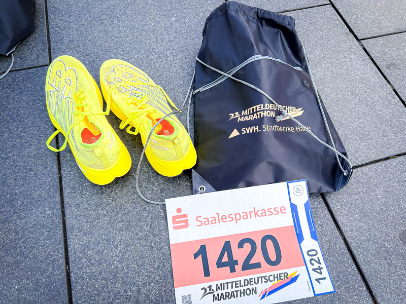 Attrezzatura per la mezza maratona - Pettorale e scarpe da corsa il giorno della gara Giorno della gara alla mezza maratona: Scarpe da corsa gialle accanto al pettorale e alla borsa sportiva del 21° Mitteldeutscher Marathon, pronti per partire.