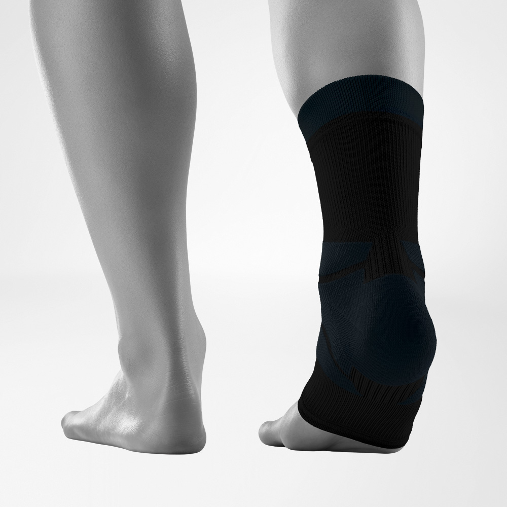 Vista posteriore di entrambi i piedi su sfondo neutro, con un piede che indossa l’Outdoor Compression Ankle Support nero. Il supporto alla caviglia avvolge saldamente l’articolazione e presenta diverse zone lavorate a maglia
