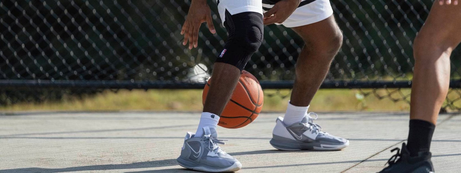 Supporto al ginocchio NBA al basket Il giocatore dribba su un campo da streetball con un basket e indossa un supporto per il ginocchio NBA nero