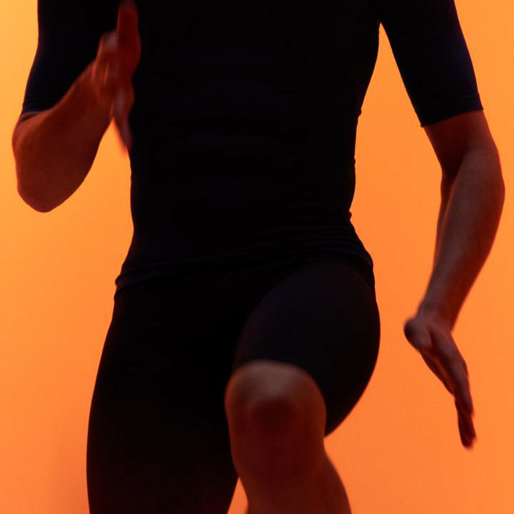 Esercizi di fitness con il nuovo indumento compressivo Bauerfeind Un uomo in abbigliamento sportivo esegue una ginocchiata davanti a uno sfondo arancione