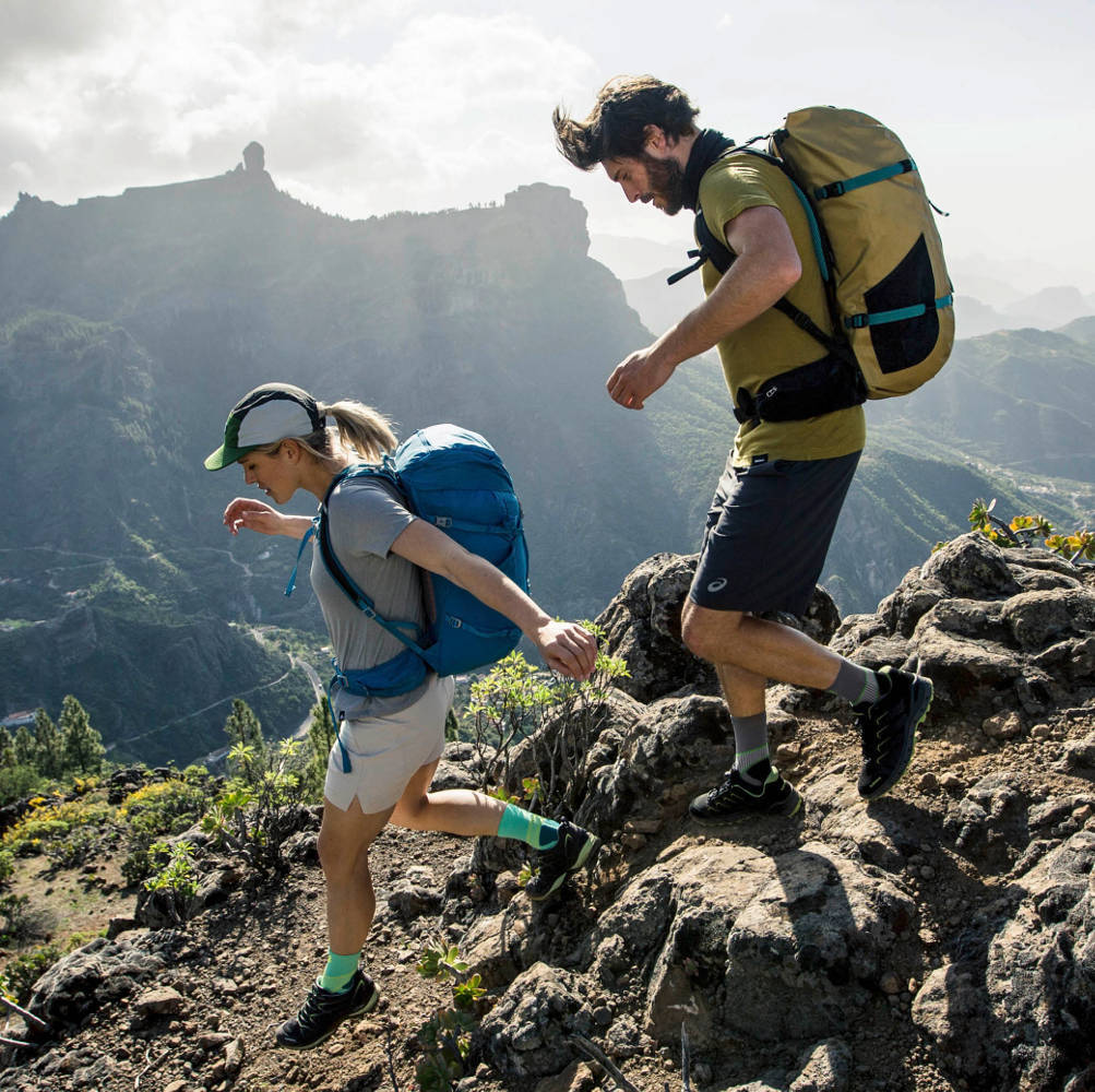Coppie con zaini grandi e calze escursionistiche di media lunghezza escursioni attraverso il terreno collinare in estate
