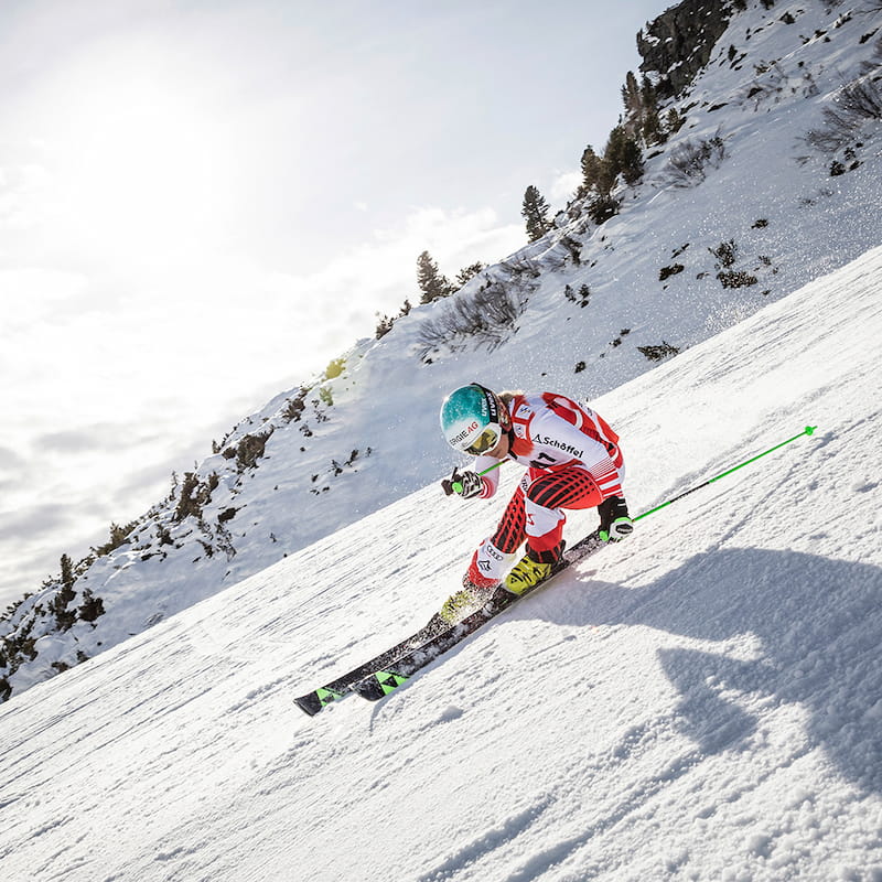 Il pilota da sci in una tuta da corsa rossa e bianca fa oscillare in un forte pendio e arbusti coperti di neve sullo sfondo con un cielo leggermente nuvoloso
