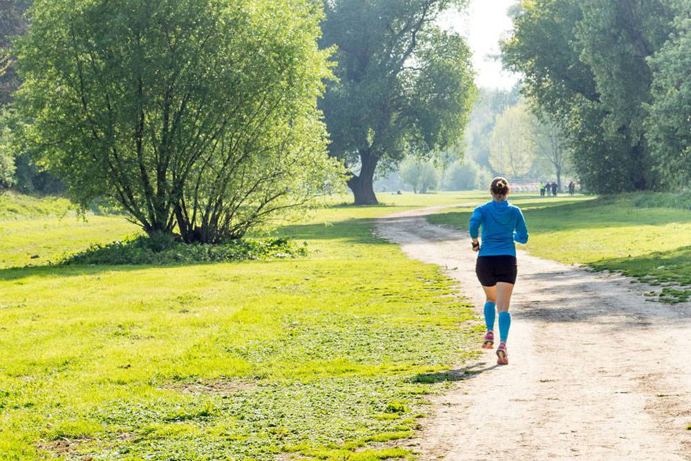 Quando arriva la primavera, il parco cittadino è uno dei posti più belli di sempre Donna con un maglione blu e le maniche blu vanno da corsa attraverso la vista sul retro del parco