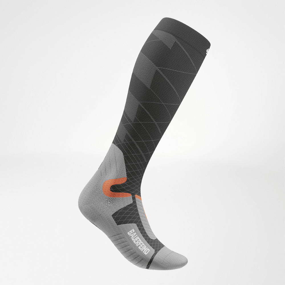 Vista laterale di una calza tecnica da sci Bauerfeind Sports fino al ginocchio, nei colori antracite, grigio e arancione. La calza compressiva presenta un design dinamico e una forma anatomica del piede.