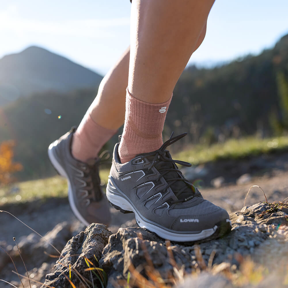 Donna che indossa le Merino Outdoor Socks color corallo durante un'escursione in montagna. Le calze si adattano perfettamente al piede e offrono traspirabilità e comfort per lunghi percorsi.