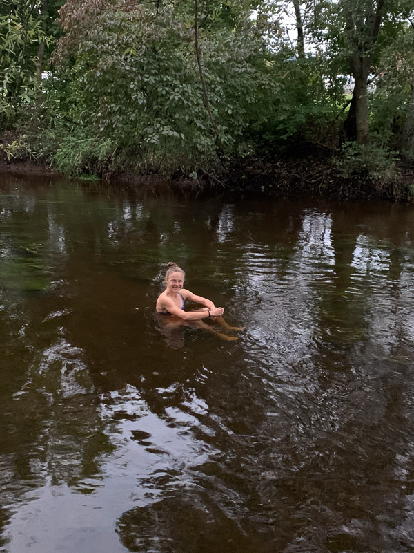 Anna Hahner nell'acqua fredda del fiume Anna Hahner nel fiume, circondata da alberi, sorridente e guardando verso la fotocamera.