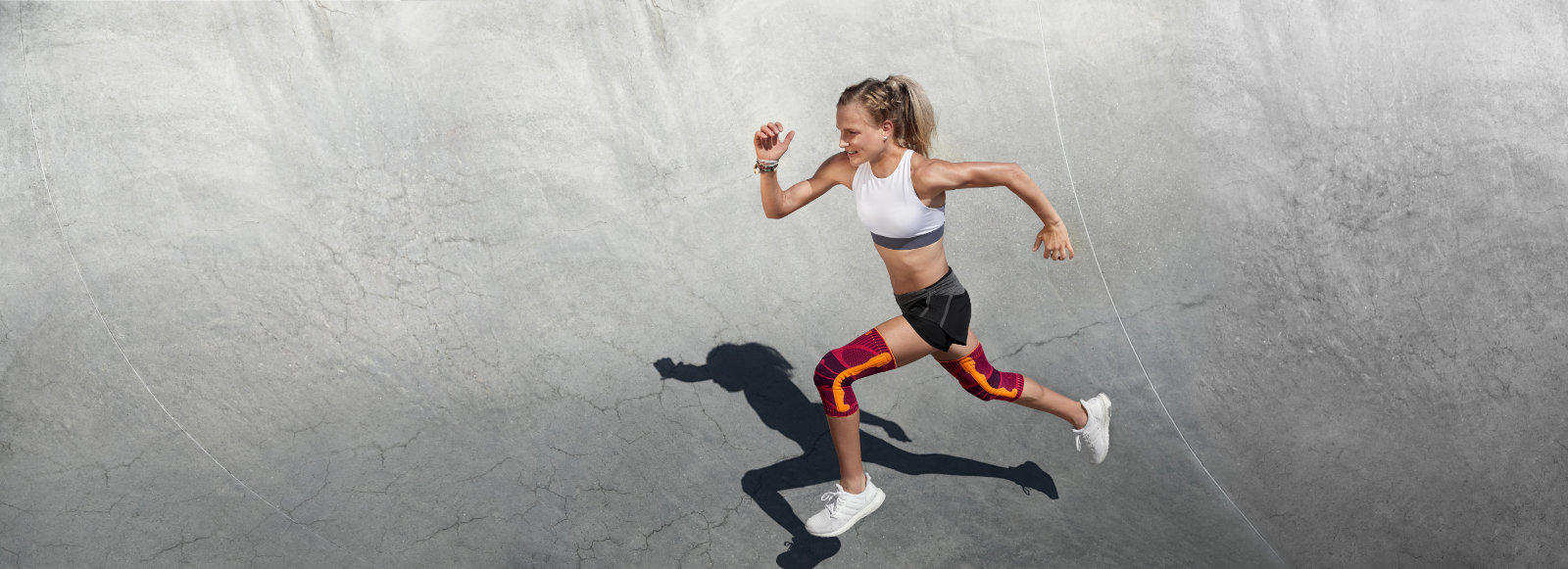 Donna in estate che corre abiti e con il ginocchio rosa corre su un halbrund di cemento