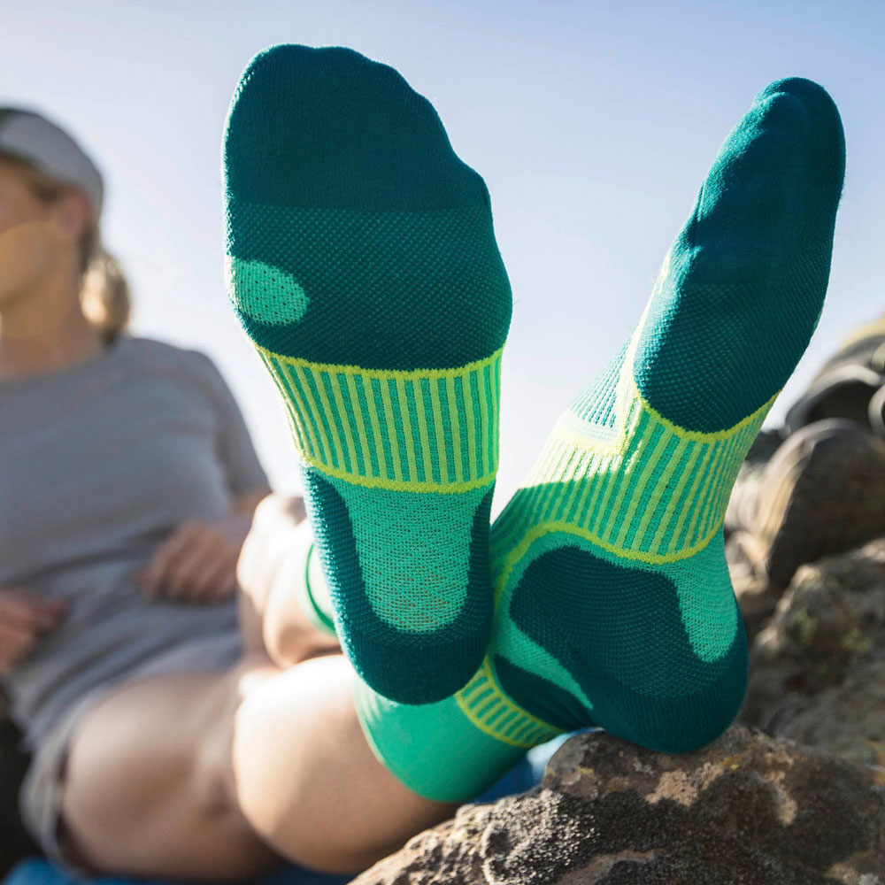 Escursionista che alza le gambe durante una pausa, focus sulle calze da trekking verdi che indossa