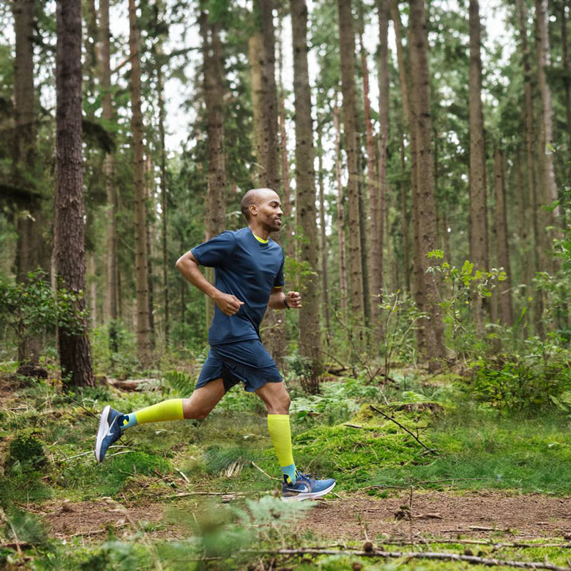 Un corridore corre veloce attraverso un fitto bosco e indossa calze a compressione