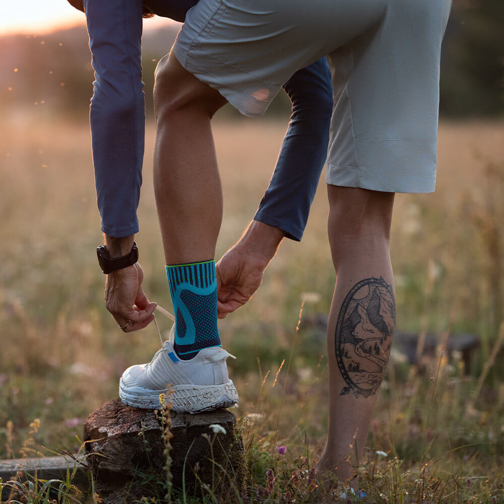 Un uomo mette il piede su un moncone e lega la sua scarpa nuova. Ha una benda di tendine di Achille sul piede sinistro