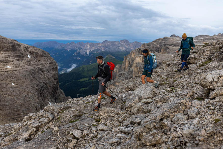 Escursionismo con vista nelle Dolomiti Tre persone in escursione nelle Dolomiti, camminando su un campo roccioso e guardando nella valle verde.