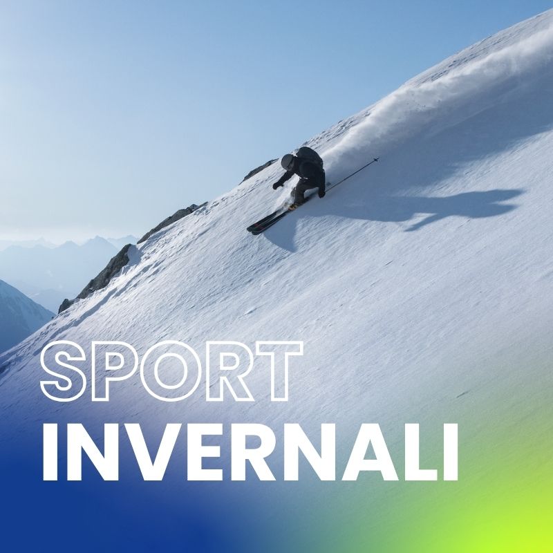 Uno sportivo invernale scende da un ripido pendio innevato lasciando una scia dinamica di neve fresca. Sullo sfondo le vette alpine si ergono maestose.