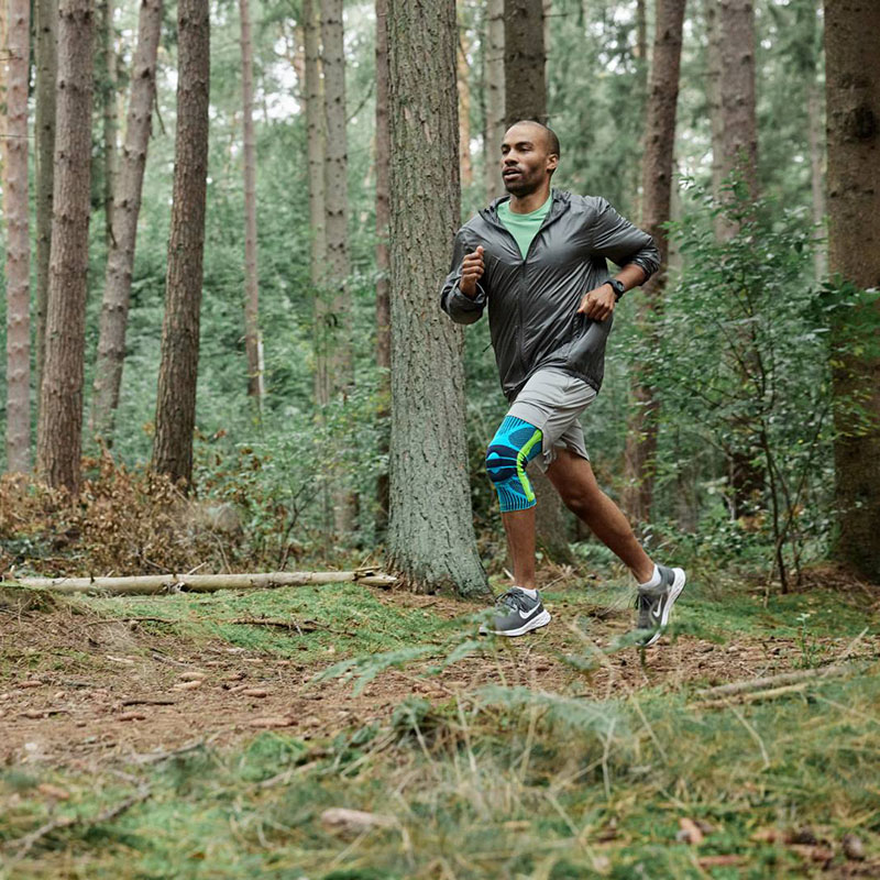 Un corridore corre dinamicamente attraverso il bosco e indossa una fasciatura al ginocchio