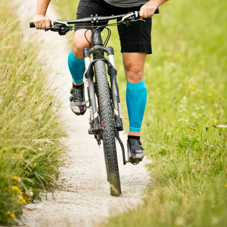 Il ciclista di registrazione frontale indossa le maniche waden mentre guida attraverso un sentiero di ghiaia sulla mountain bike