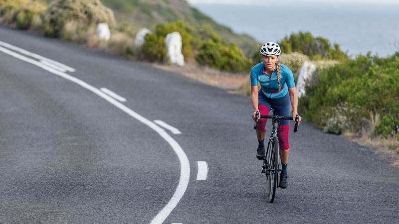 Donna con armi e fascette sullo sfondo dell'immagine corre su una mountain bike su un sentiero tra l'erba alta