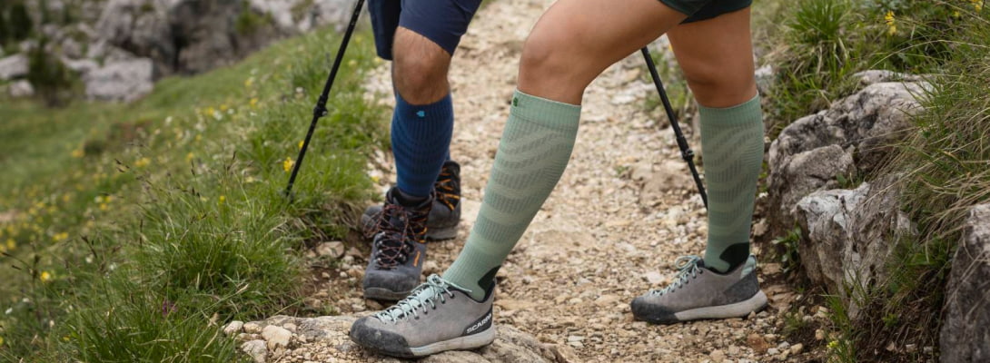 Calzini da escursioni blu merino durante le escursioni Due persone che fanno un'escursione sulle rocce indossano calze da trekking merino sullo sfondo possono essere visti alberi