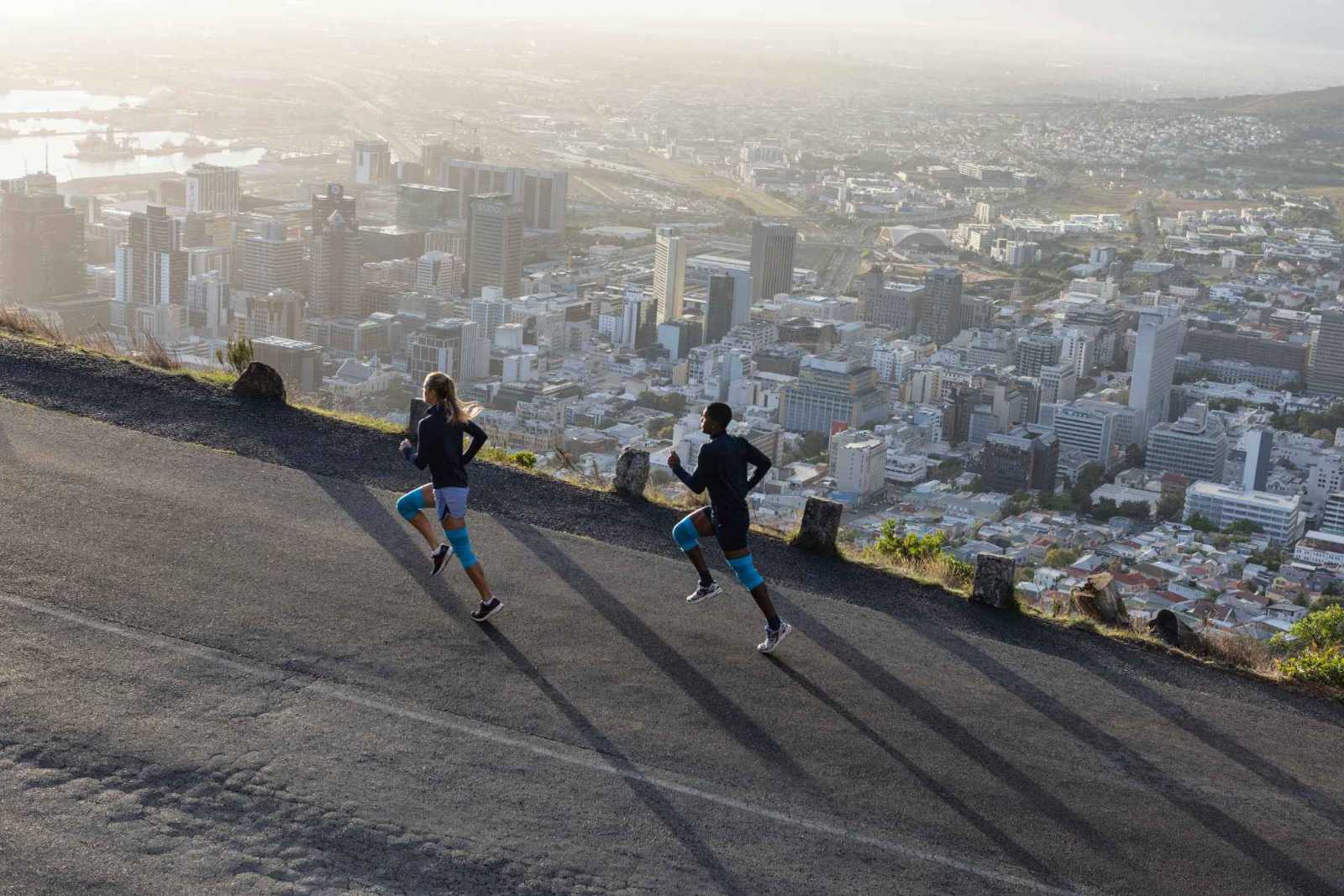 Una donna e un uomo con le barre del ginocchio blu corrono su una strada sopra una grande città