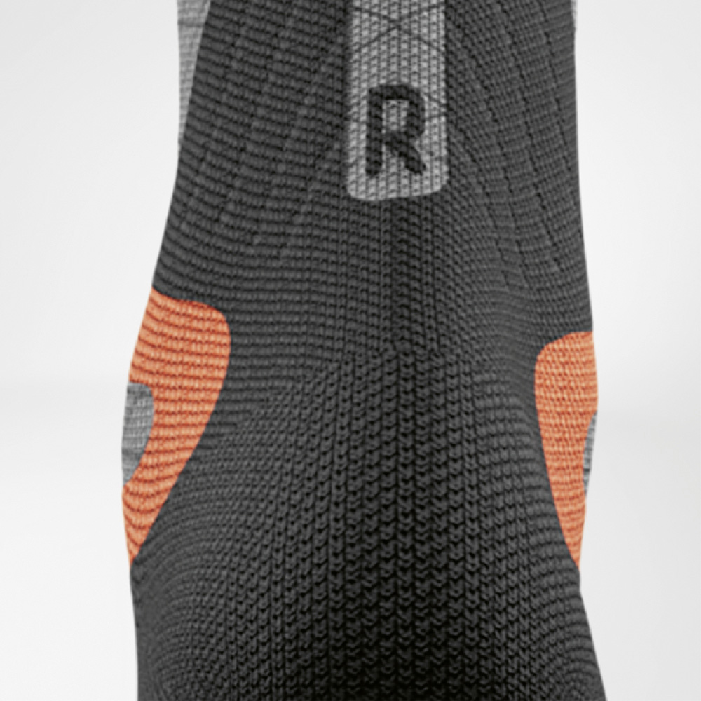 Stabilità in ogni curva – tallone destro con imbottitura extra Vista dettagliata della calza compressiva da sci destra per donna Bauerfeind. Visibili i cuscinetti arancioni sul tallone e la struttura a maglia nera per un supporto mirato.