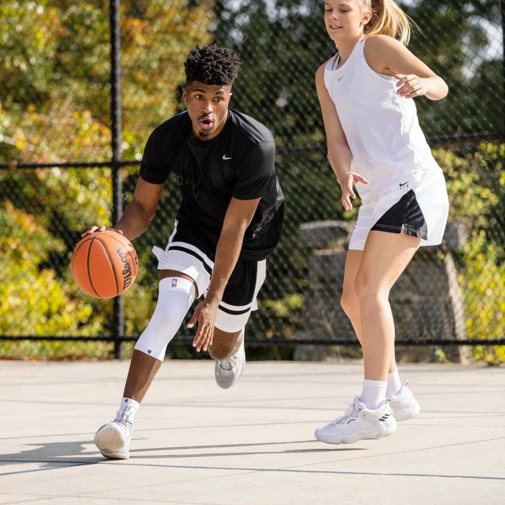 Due giocatori di basket in un duello uno contro uno su un campo all'aperto. Il giocatore in nero indossa una ginocchiera a compressione bianca e palleggia, mentre l'avversario in bianco difende.