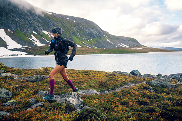 Johanna Aström corre lungo le pietre lungo un lago con una giacca con cappuccio