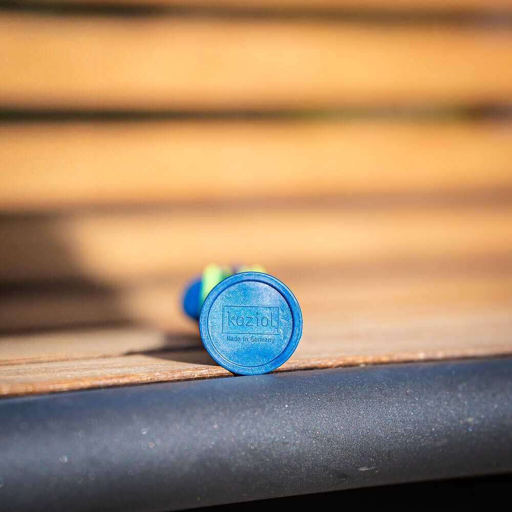 Made in Germany: Dettaglio di posate sostenibili Primo piano del fondo di una posata blu sdraiata su una panchina di legno. Sul fondo è presente il logo "Koziol Made in Germany."