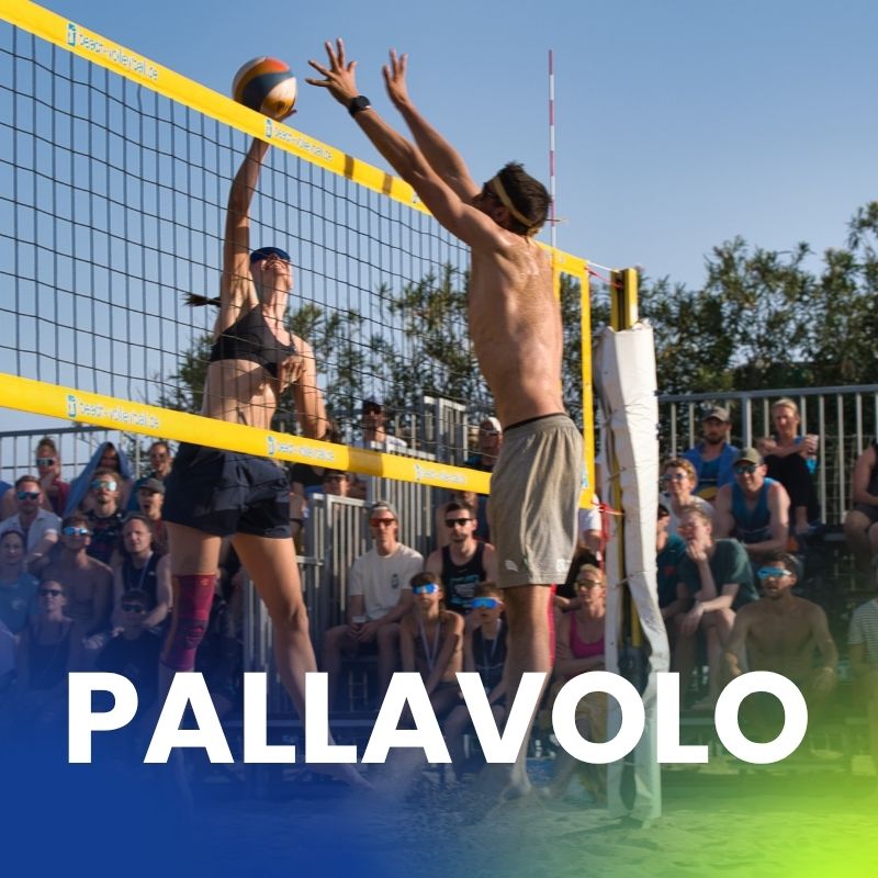 Una giocatrice di pallavolo salta per un attacco mentre un avversario maschile cerca di bloccare. Il pubblico segue la partita con attenzione.
