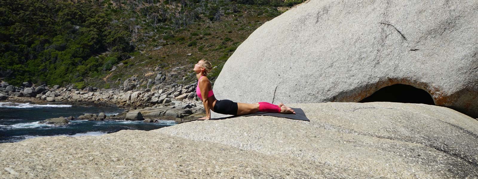 Yoga all'aperto - Pink della parte inferiore della gamba sportiva La donna fa esercizi di yoga su una grande roccia sull'acqua e le maniche rosa della parte inferiore della gamba
