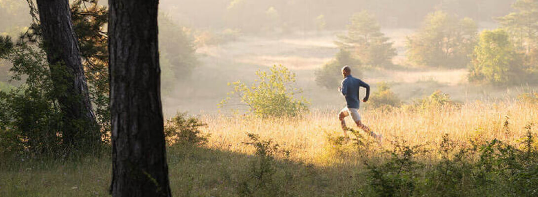 L'uomo jogging sopra un prato in primo piano un albero sullo sfondo sono colline