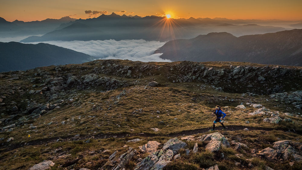 Ultrarunner su un sentiero di montagna all'alba con vista sulle Alpi