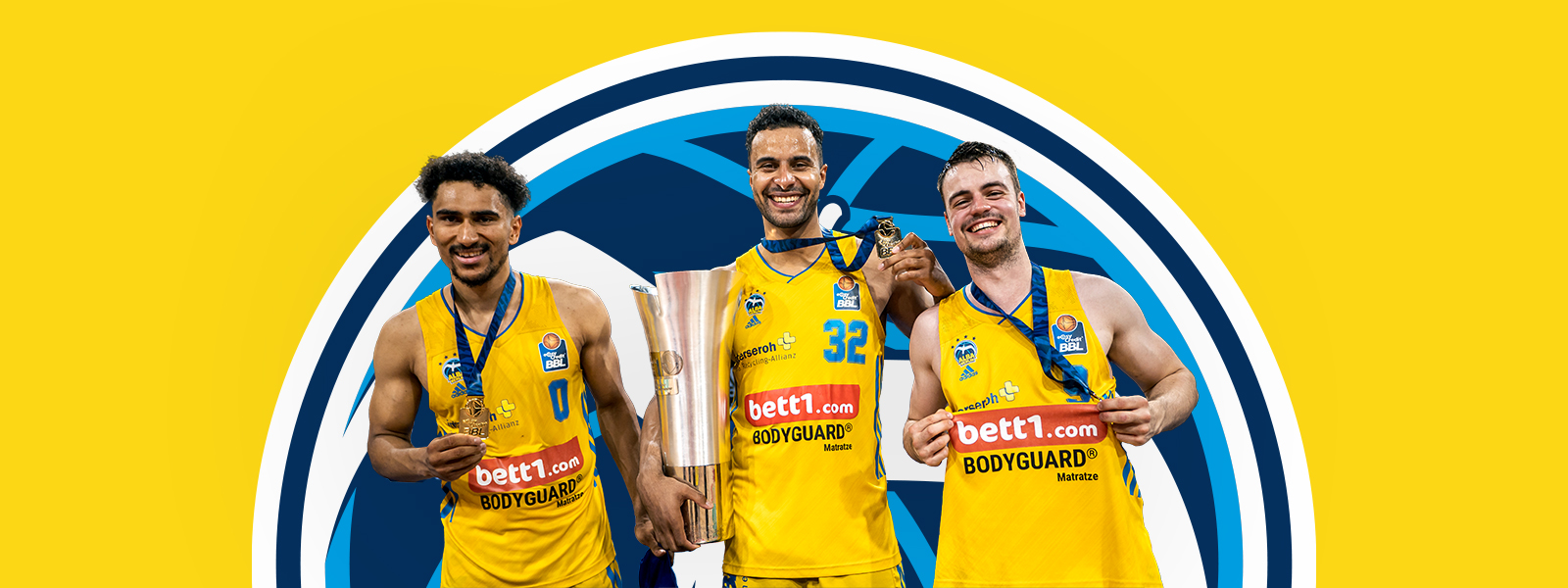 Tre giocatori di Alba Berlin con un trofeo di fronte a un'area gialla con il logo Alba Berlin