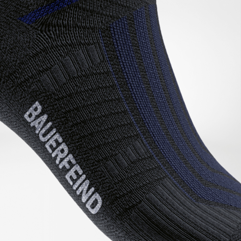 Nero e blu: performance con stile. Vista laterale della calza Run Performance Midcut nera con sottili righe blu e scritta bianca “BAUERFEIND” sul piede.