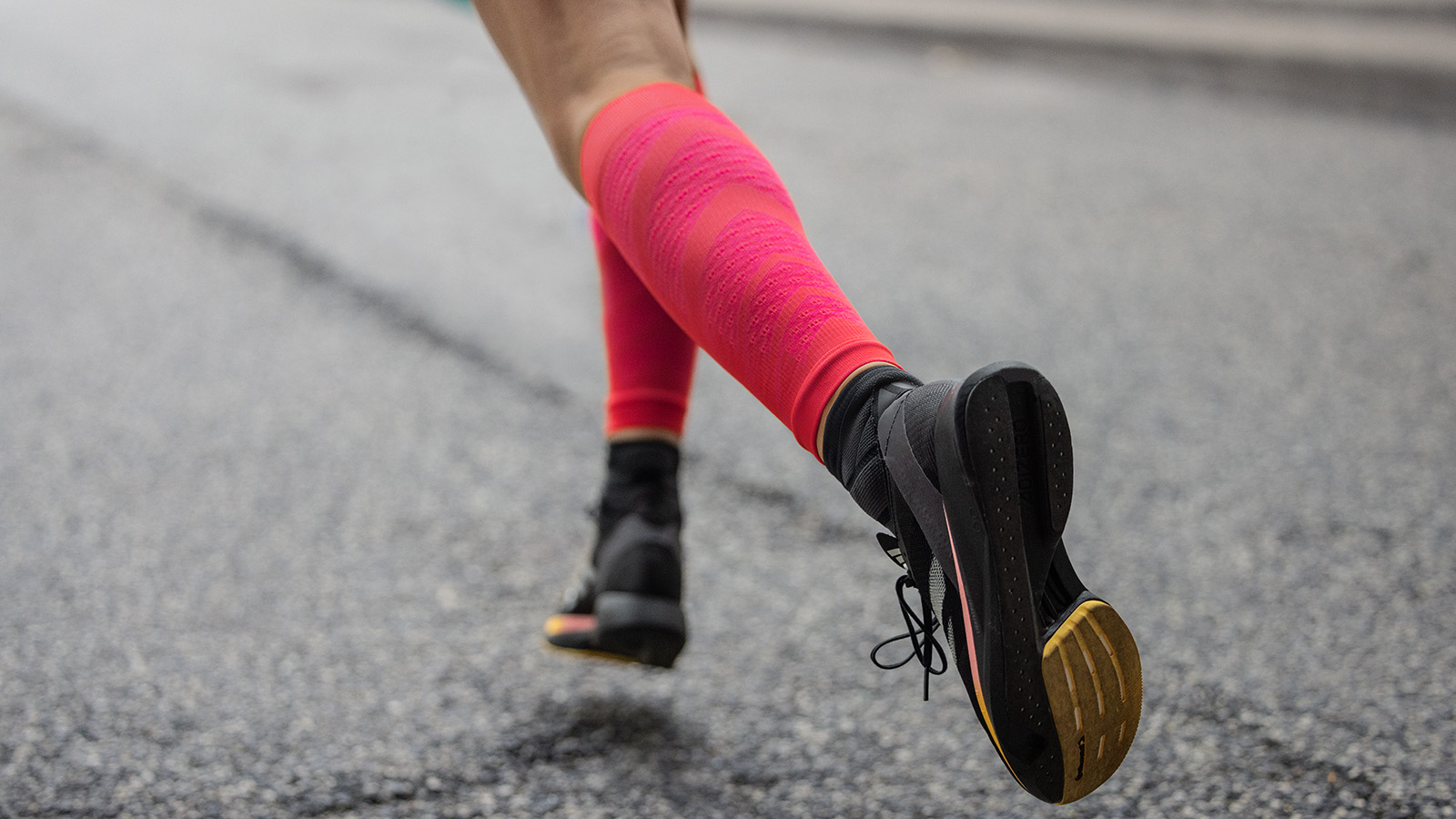 Close Up: calzini da corsa rosa lunghi e scarpe da corsa nere corrono su una strada asfaltata in una città